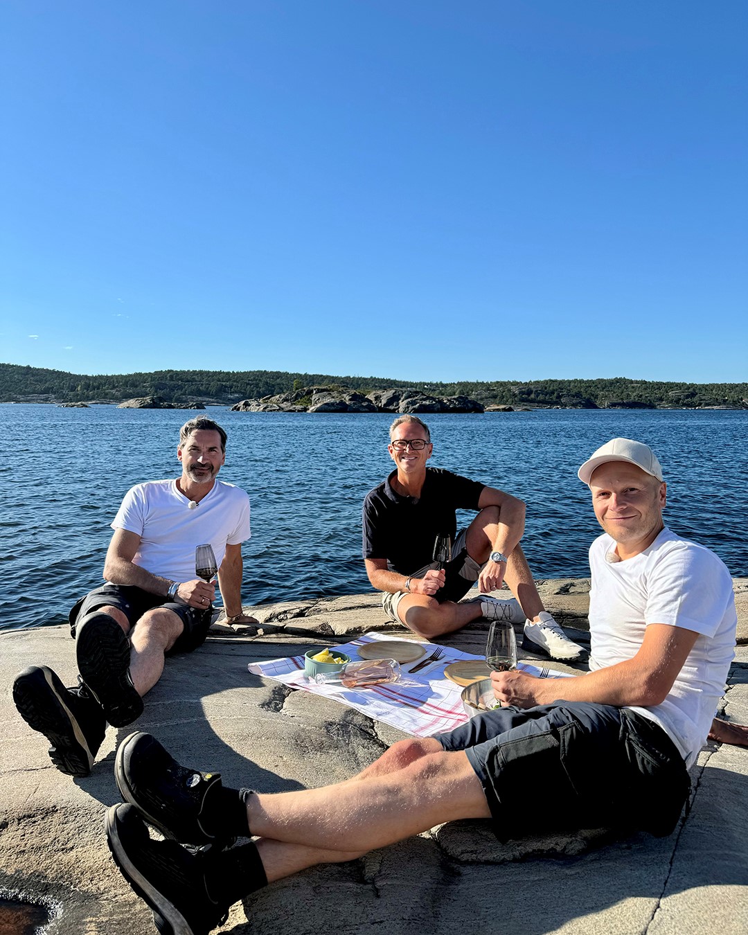 Halvor Bakke og snekkerne sitter og spiser og drikker på svaberg med sjøen i bakgrunnen.  Fra Eventyrlig Oppussing 2024 Portør. Foto.