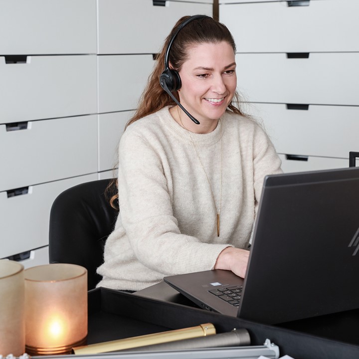 Ansatt hos Gardinmaker.no som sitter ved laptop og veileder kunde. I forgrunnen ser vi prøver på gardinoppheng og tekstiler. Foto.