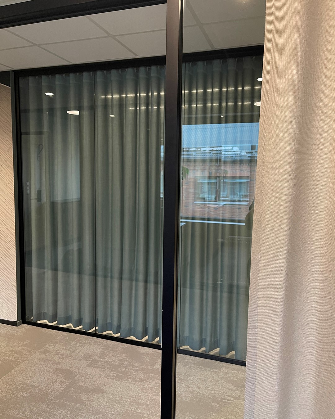 Vi ser utsiden av et møterom med glassvegger og gardiner som skjerming. Foto.